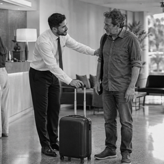 Profissional de hotelaria acolhe e auxilia um hóspede recém-chegado no lobby do hotel.