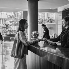 Equipe de hotel acolhe uma hóspede na recepção, dando vida e significado ao empreendimento.