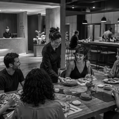 Hóspedes compartilham uma refeição em restaurante integrado ao lobby de um hotel contemporâneo.